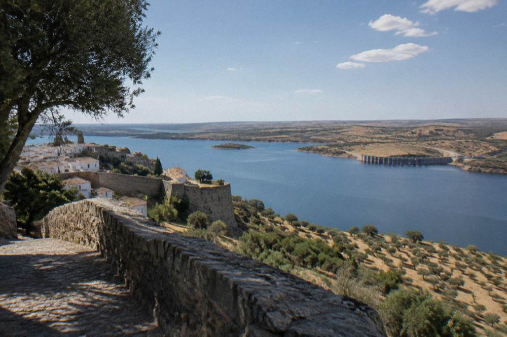 Stone ramparts of Monsaraz village above the blue expanse of the Alqueva reservoir at late afternoon