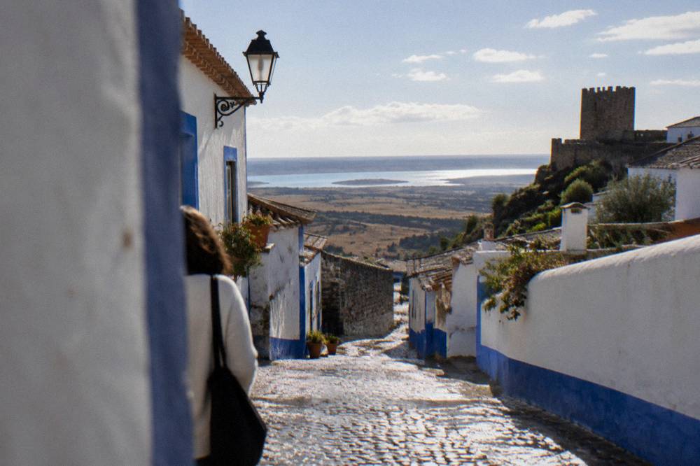 Whitewashed street in Monsaraz with blue trim and a view opening toward the reservoir