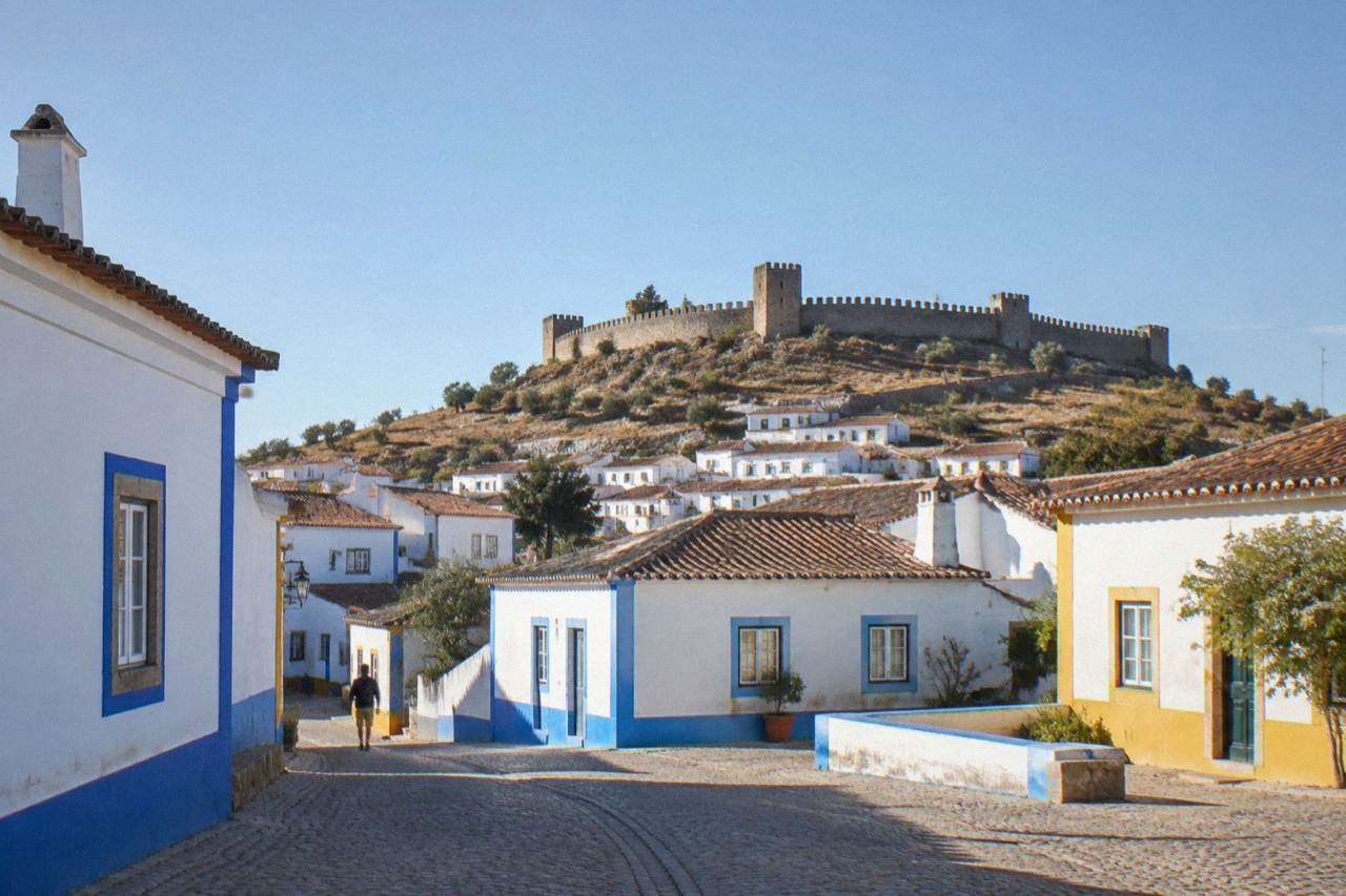 White Alentejo houses with blue and yellow trim below a hilltop castle wall under a clear sky