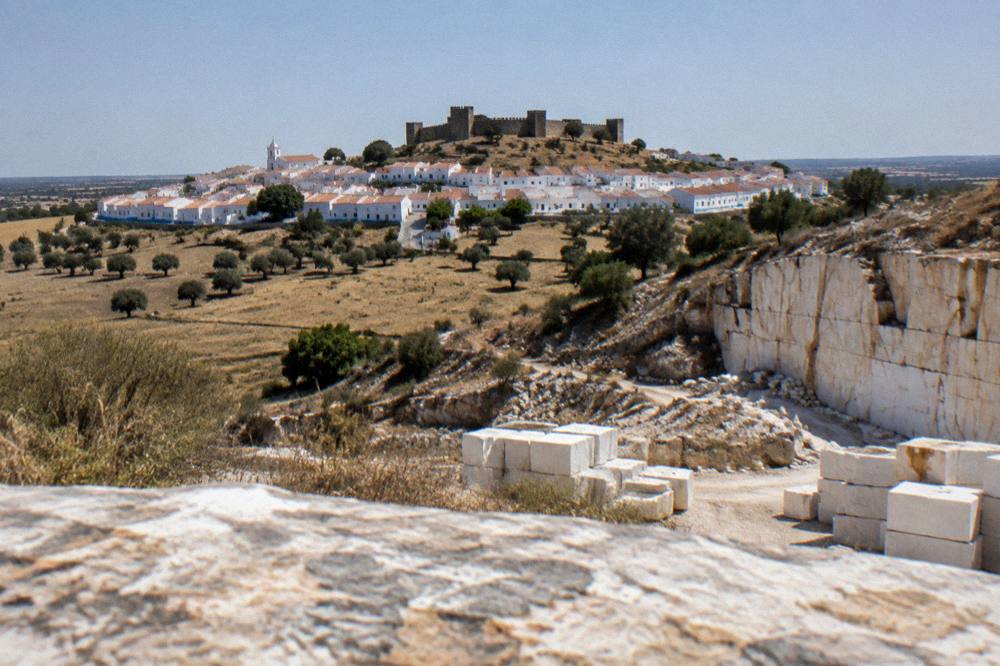 A stone quarry face cut into a hillside with pale marble blocks stacked nearby