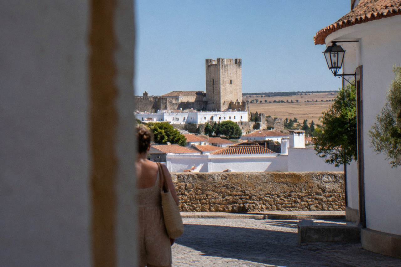 A stone castle keep rising above whitewashed houses under a wide blue sky on the Alentejo plain