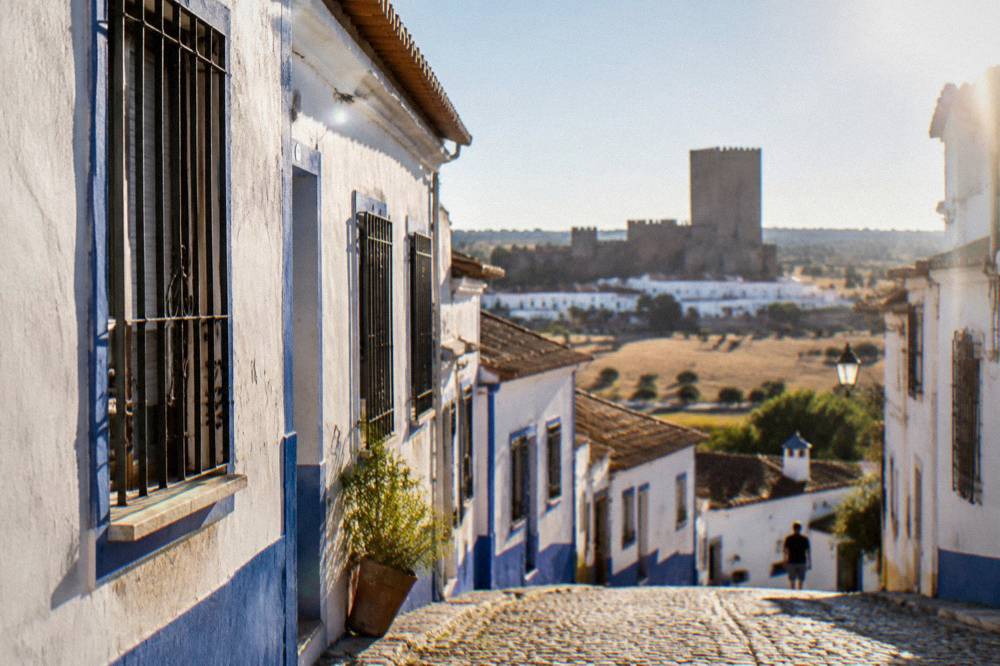 A narrow street of whitewashed houses with blue painted trim and iron window grilles in a southern Alentejo town