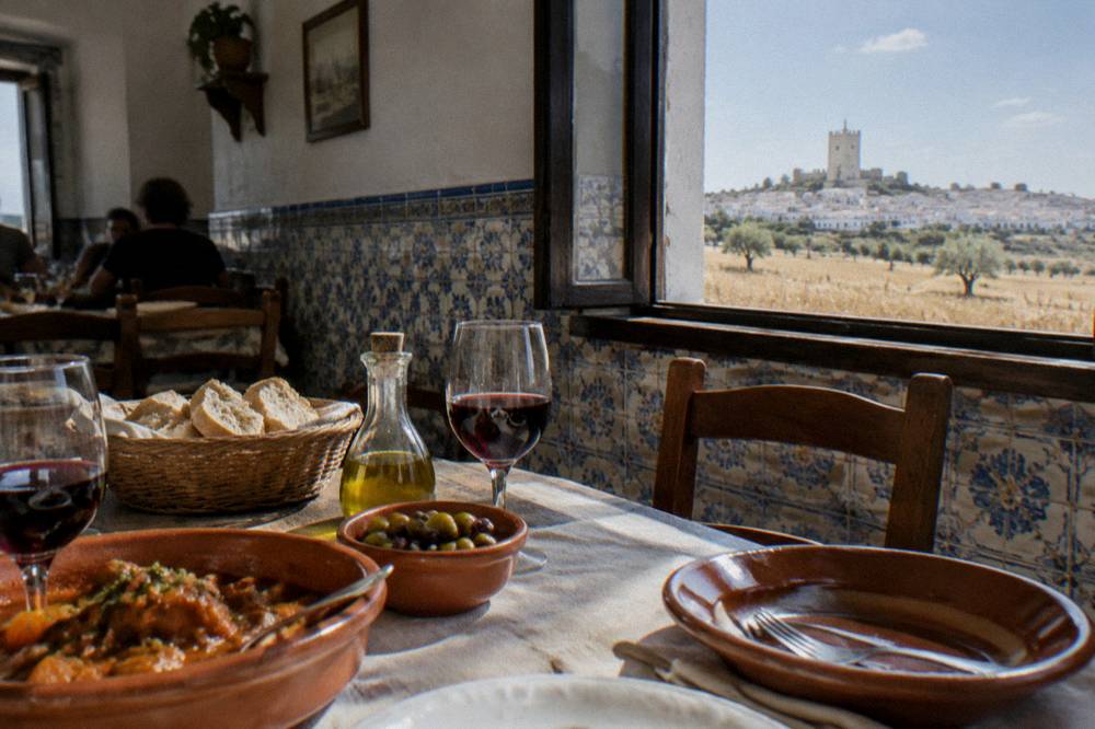 A rustic Alentejo lunch table with bread, olive oil, wine glasses and clay dishes in a tiled tavern room