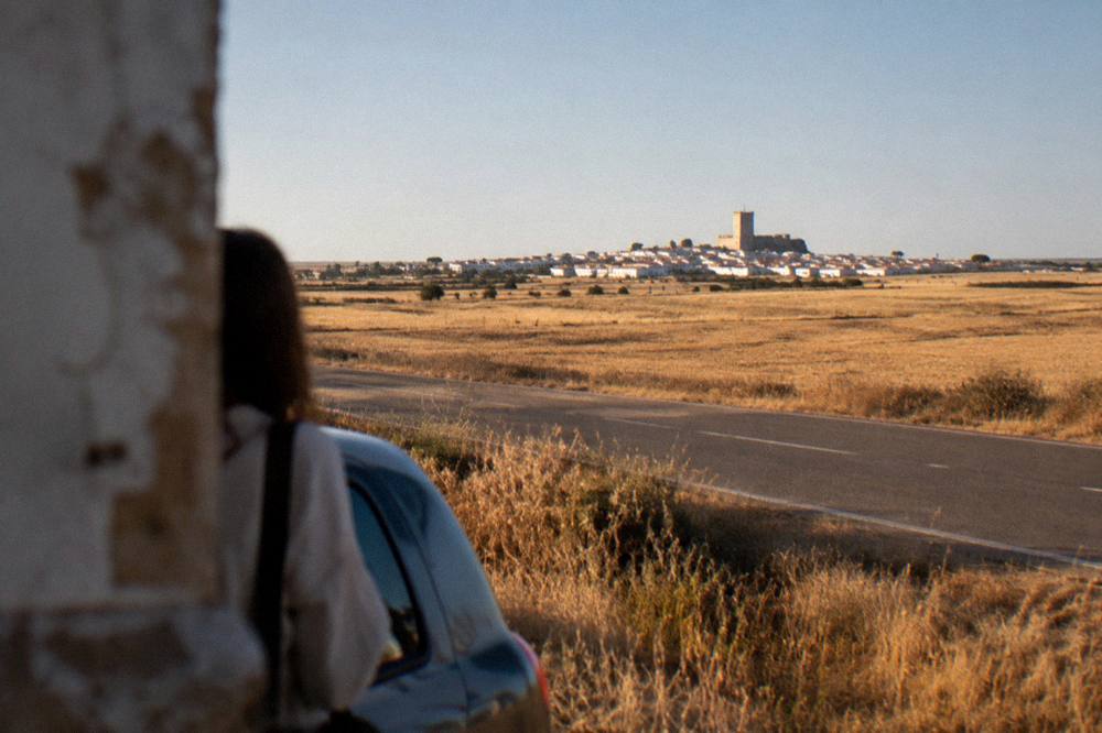 An empty road running straight across a golden plain toward a distant town on the horizon