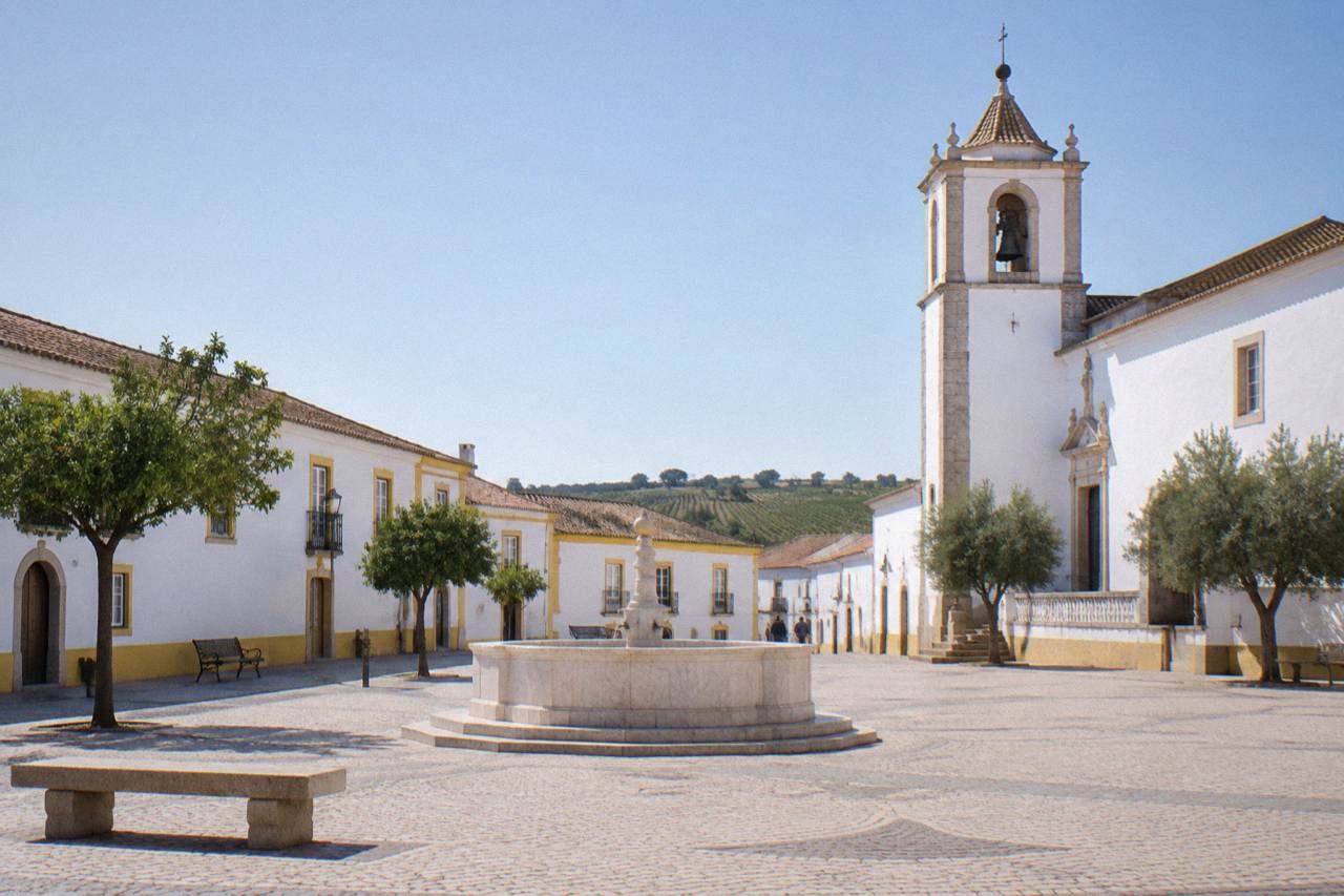 A quiet Alentejo town square with whitewashed buildings and a church tower under a clear sky