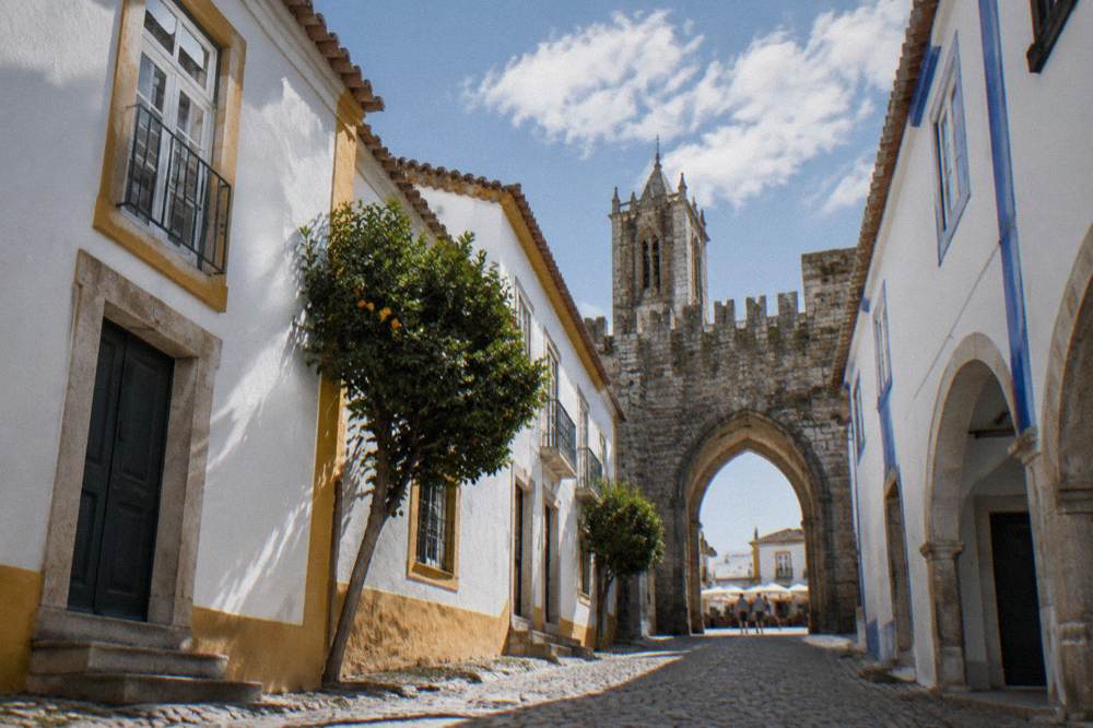 Stone archway leading from a lively square into a walled old town with towers above