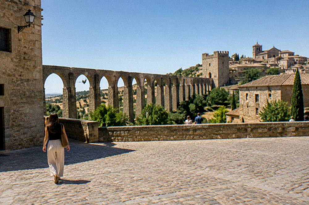 Tall stone aqueduct arches stretching across countryside toward a hilltop town
