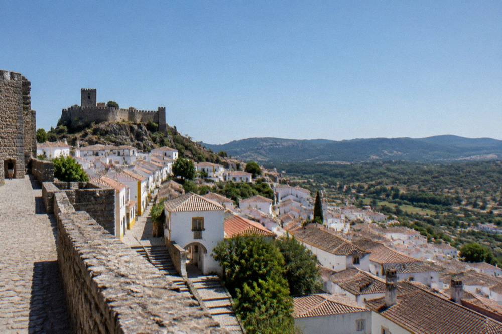 Panoramic view over whitewashed rooftops and green hills from a castle wall