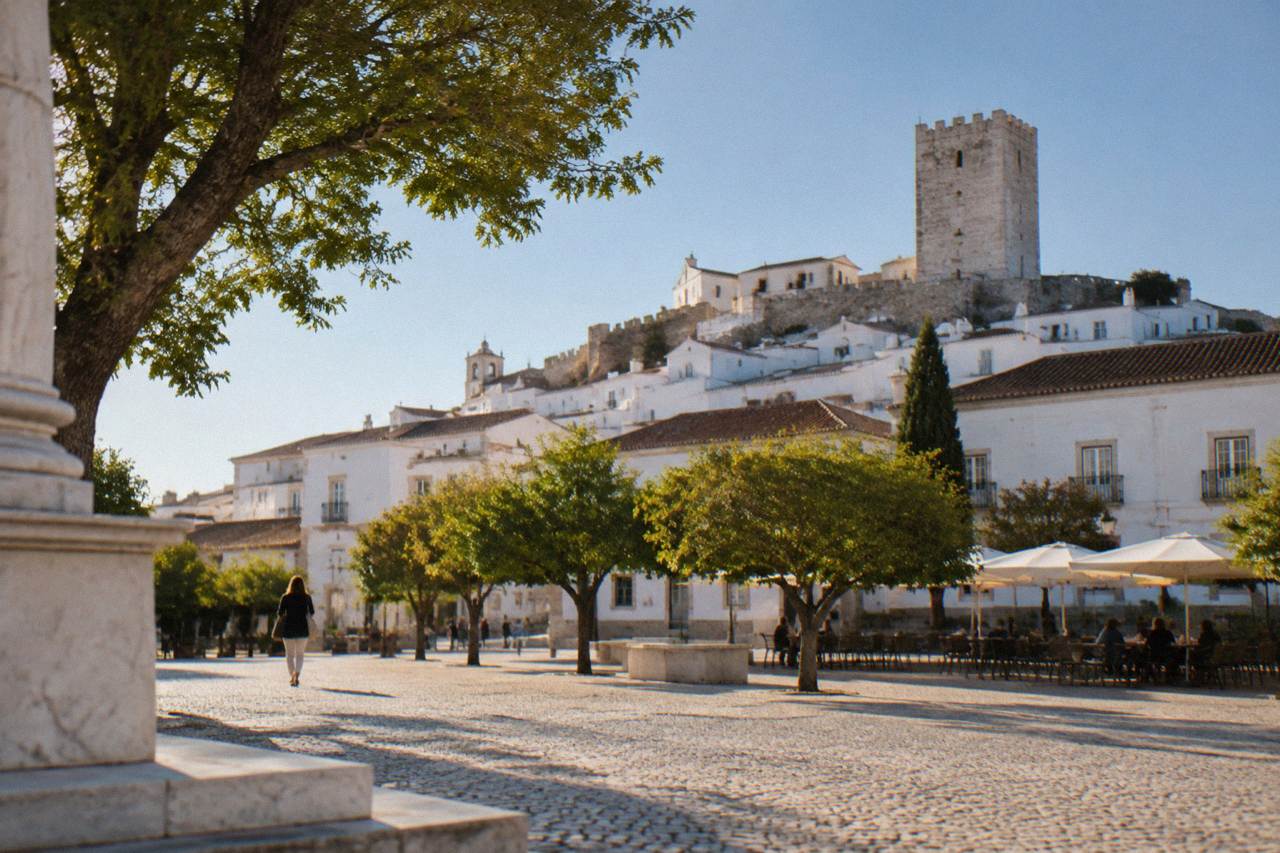 A marble-built town on a hill above the Alentejo plain, with a castle tower rising over white houses under a blue sky.