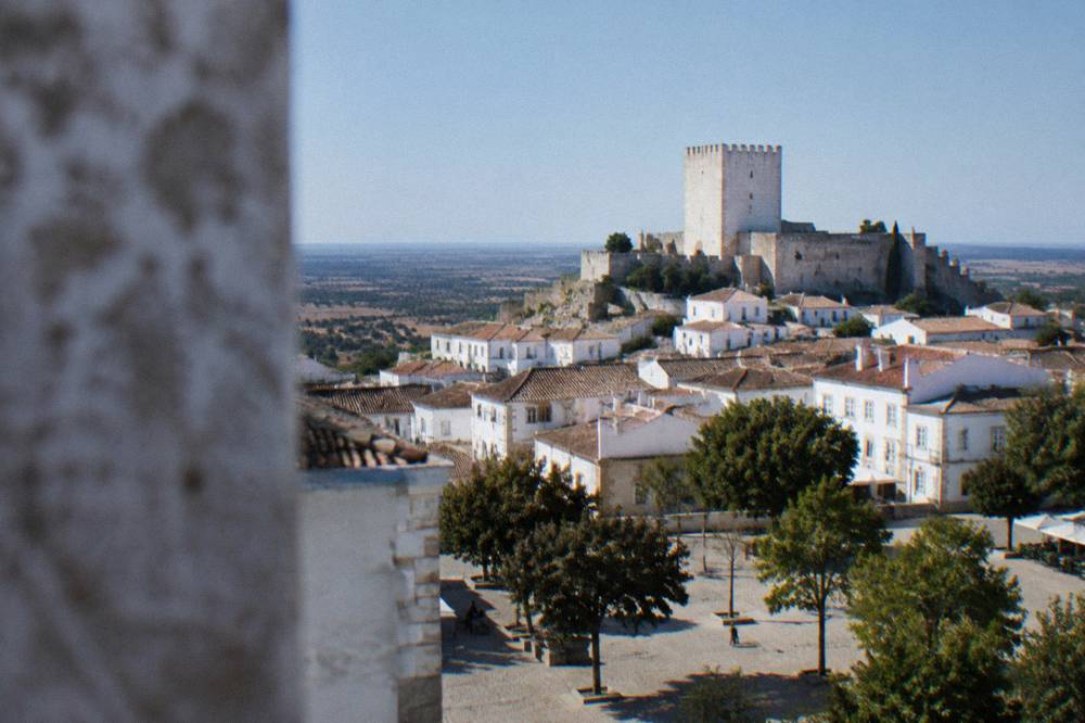 The stone keep and walls of Estremoz castle standing above tiled roofs, with the flat Alentejo plain stretching to the horizon behind.