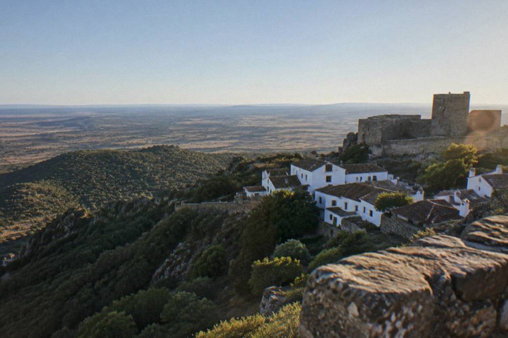 Panoramic view from castle battlements over wooded hills fading toward a distant plain