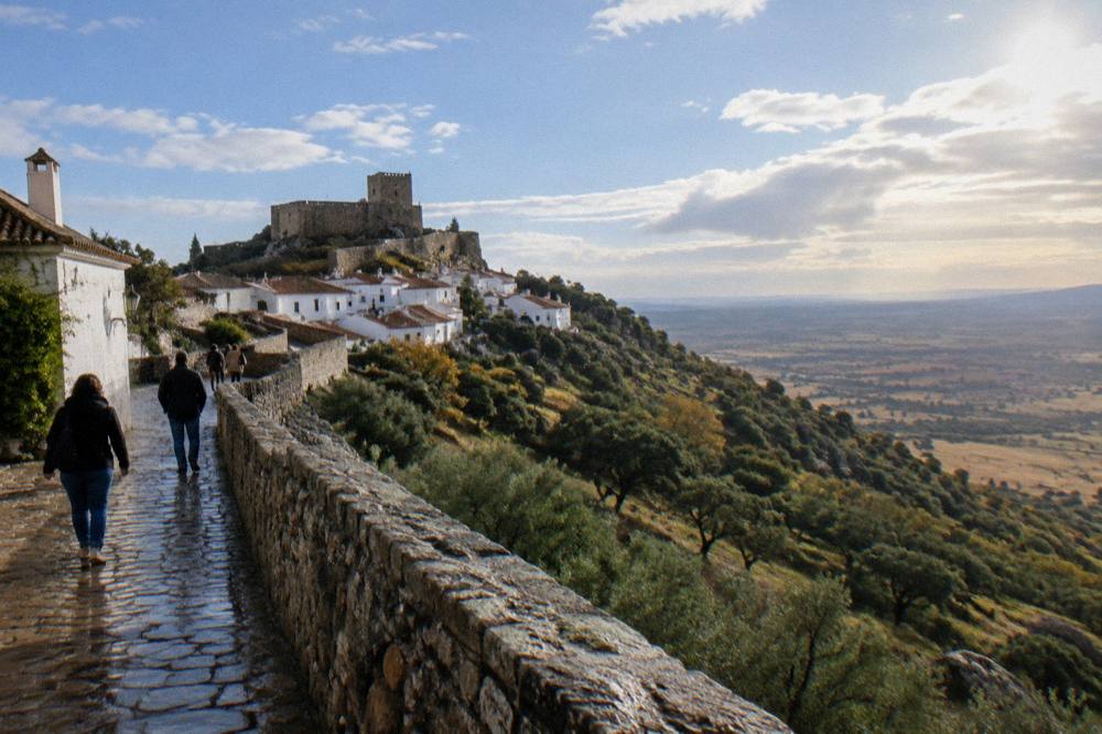 Visitors walking a stone rampart path with the village walls on one side and open country beyond