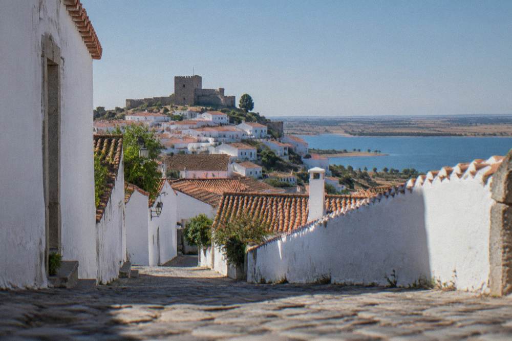 A stone castle keep with a flag above rooftops seen from a narrow lane