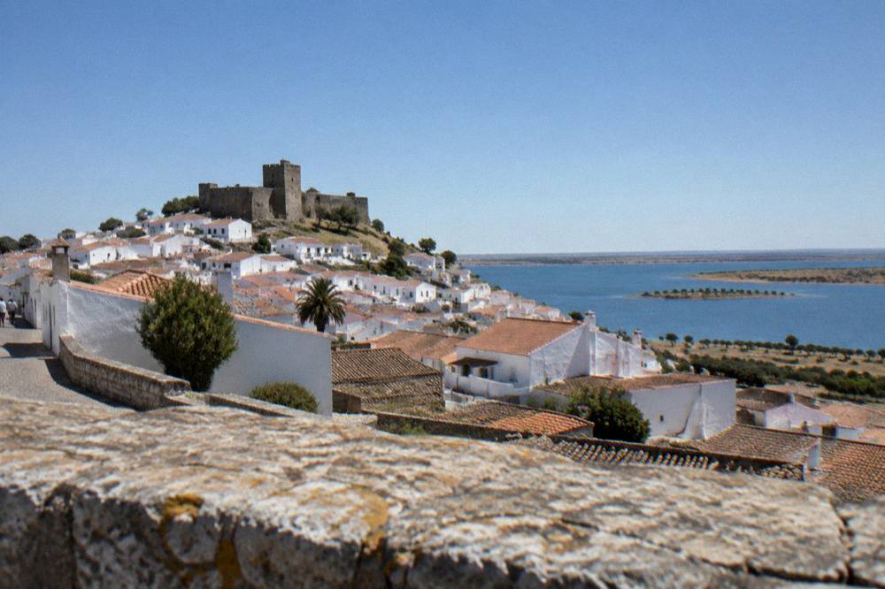 Sunset over a walled Alentejo town with rooftops and a church tower silhouetted against an orange sky