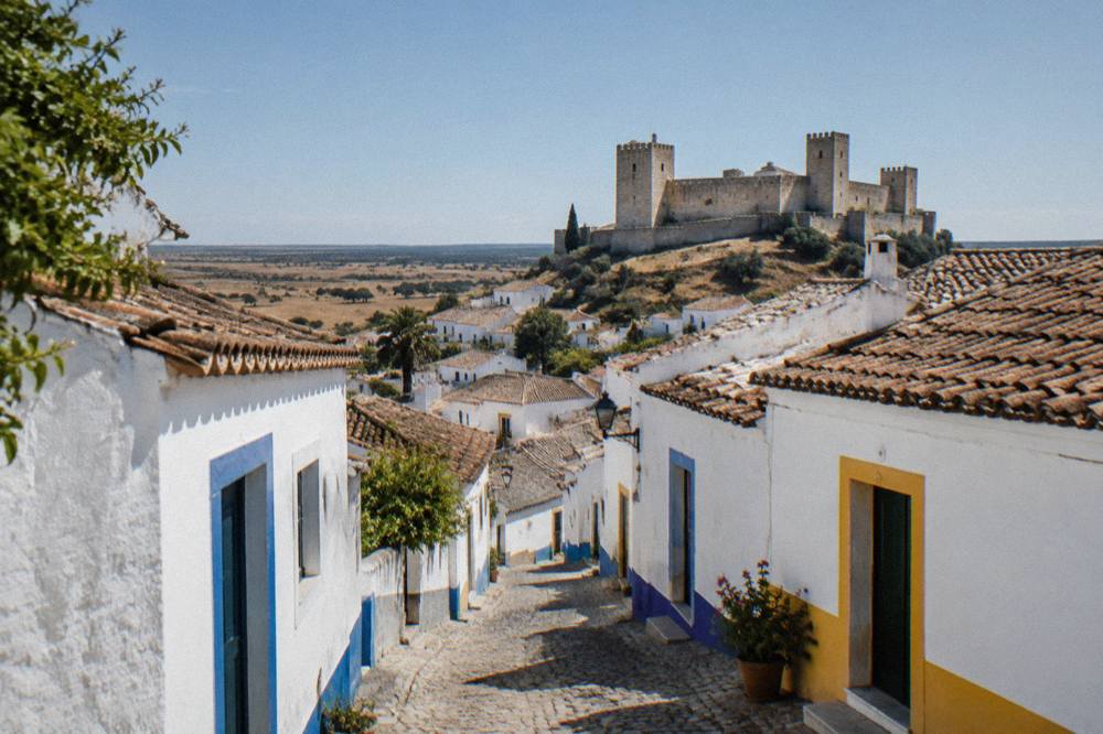A narrow whitewashed street in an Alentejo village with blue and yellow trim on the doorways