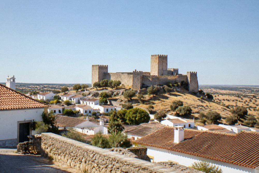 The stone walls and towers of a hilltop castle above Alentejo countryside at golden hour