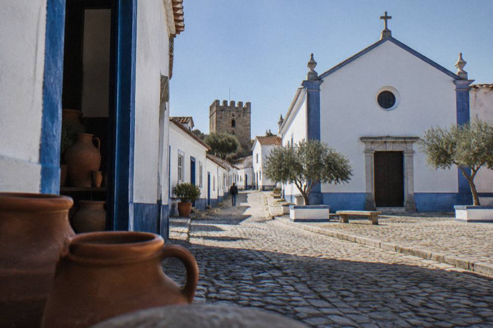 A narrow street of whitewashed houses with painted blue borders leading toward a small castle tower
