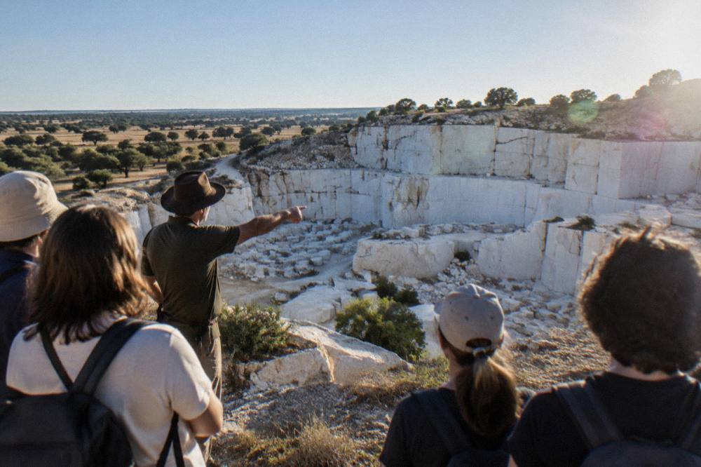A guide pointing out features of a white marble quarry face to a small group of visitors