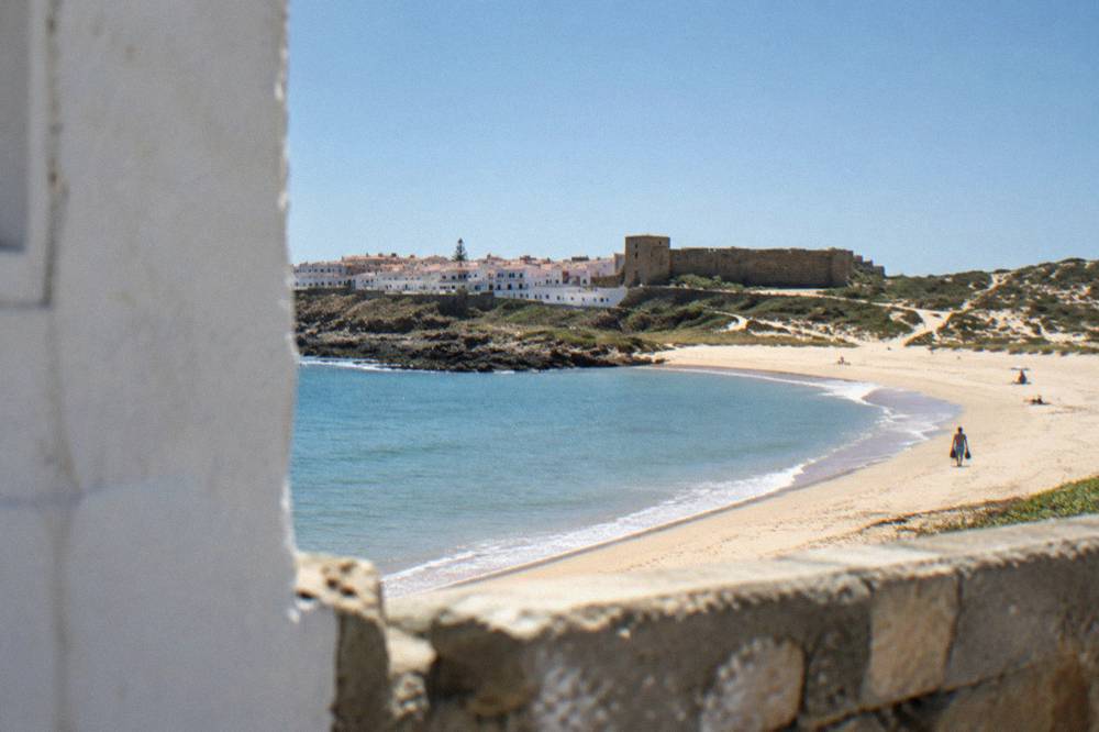 A sandy beach in a cove with calm Atlantic water and low dunes behind it