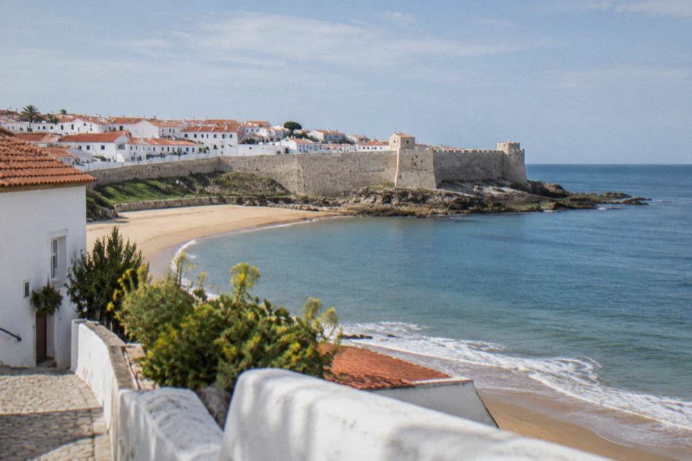 Whitewashed streets and a stone castle wall above the sea in a small Portuguese coastal town