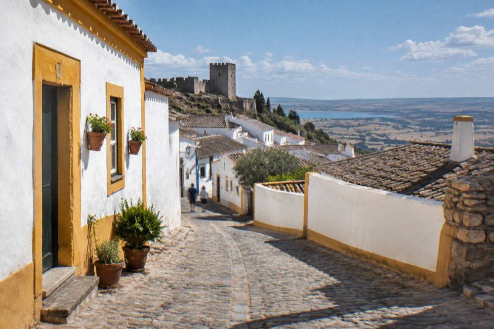 A cobbled street inside a walled Alentejo village with whitewashed houses and yellow trim