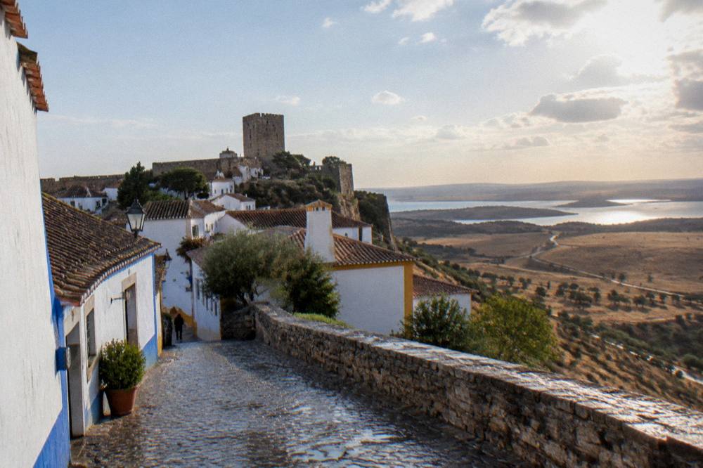 A country road crossing dry golden plains toward a distant hilltop village