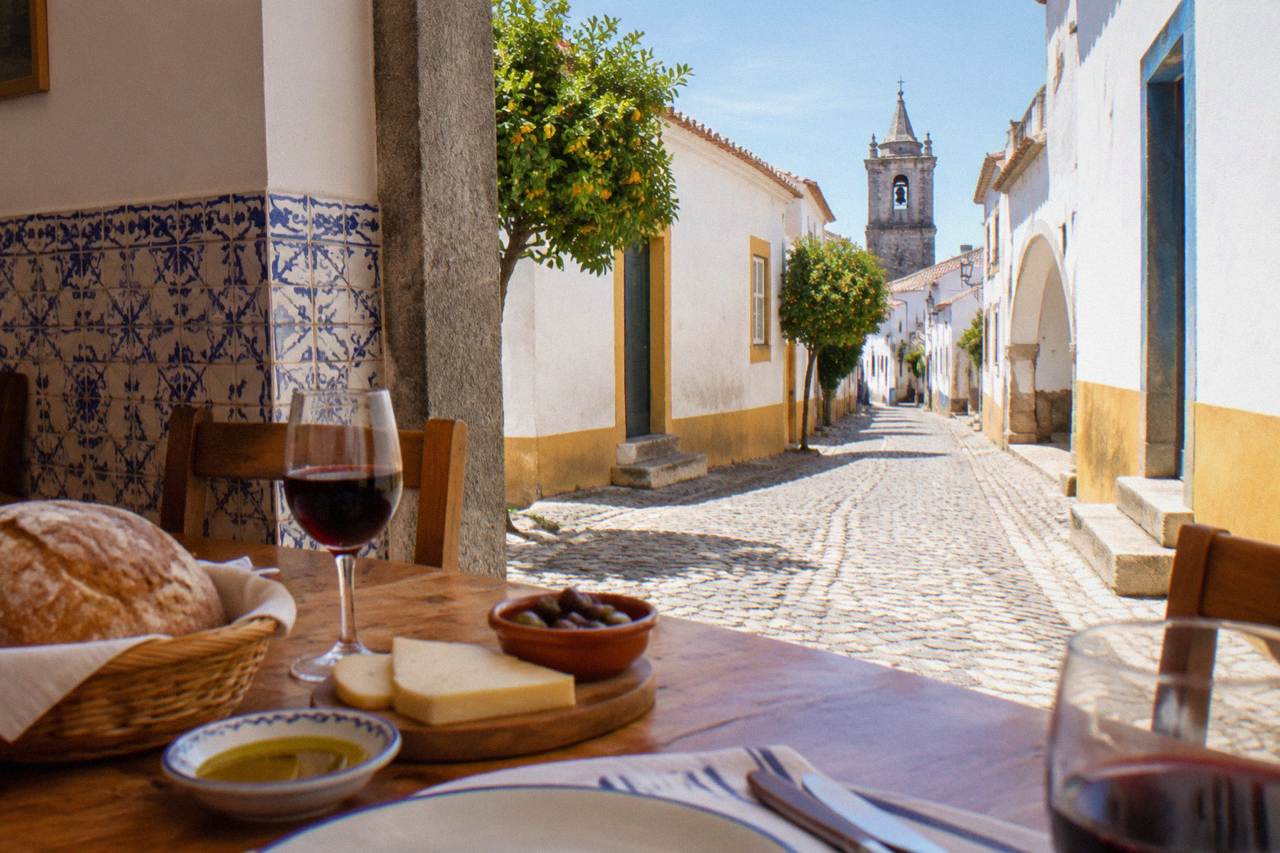 A rustic Alentejo table set with bread, olive oil, cheese and red wine in a tiled dining room