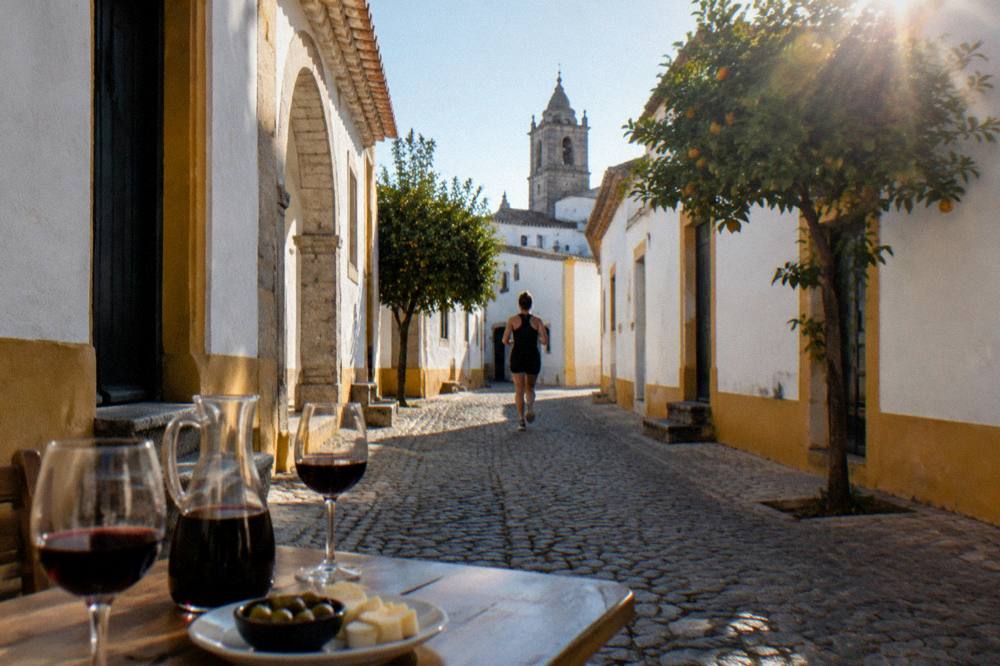 Glasses of red wine and a carafe on a table beside a plate of olives and cheese