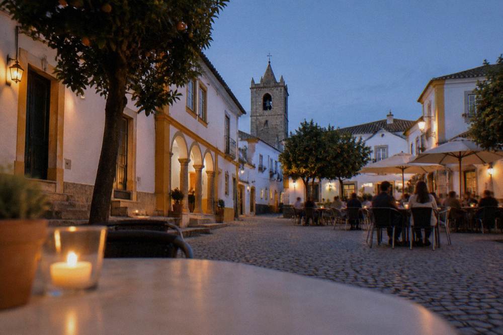 Evening diners at outdoor tables in a small Évora square lit by warm lamps