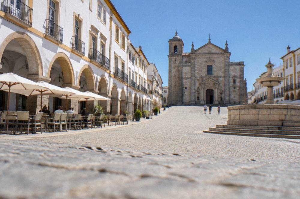 The arcaded Praça do Giraldo in Évora with café tables under the arches and the Renaissance fountain at one end