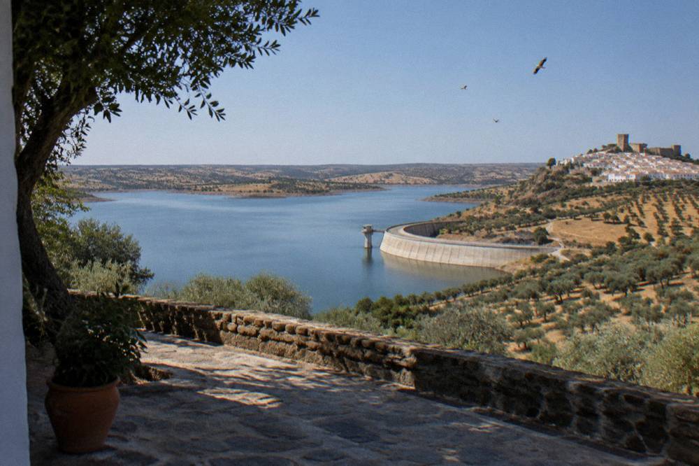The whitewashed hilltop village of Monsaraz overlooking the Alqueva reservoir at dusk with storks flying over the plain