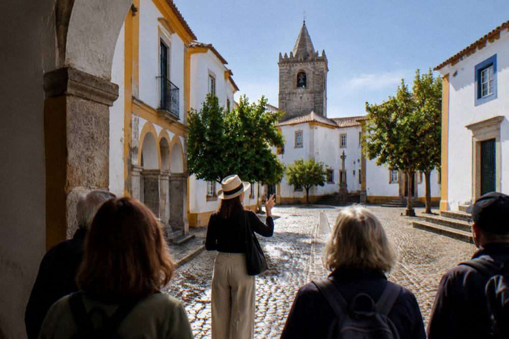 A guide leading a small walking group through a cobbled square in Évora's historic centre on a warm morning