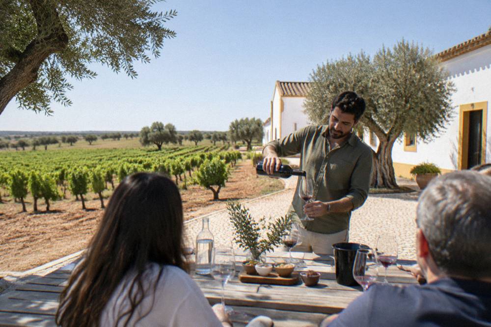 A guide pouring red wine for a small group at an outdoor tasting table in a winery courtyard