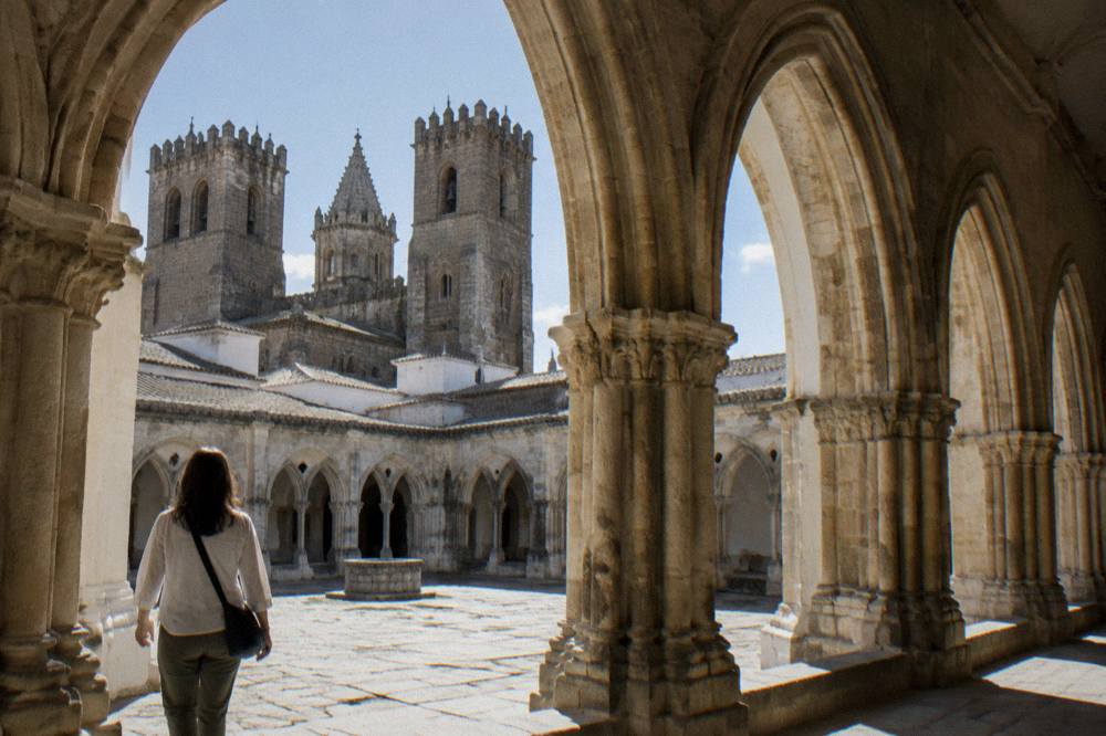 A visitor walking through the cloister of Évora cathedral with sunlight on stone arches