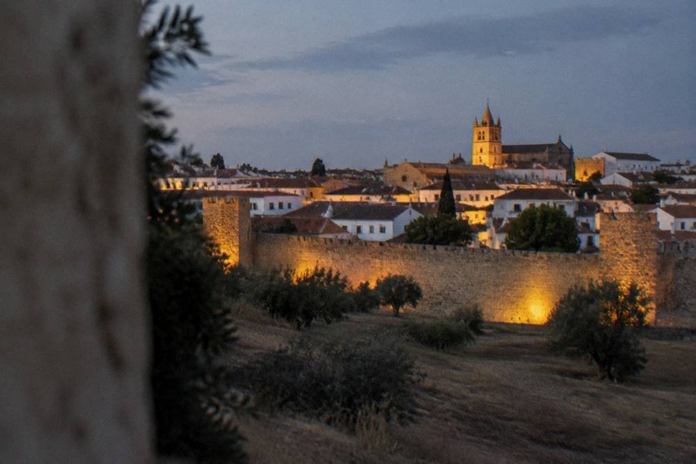 The floodlit walls and rooftops of Évora seen at dusk from outside the old city