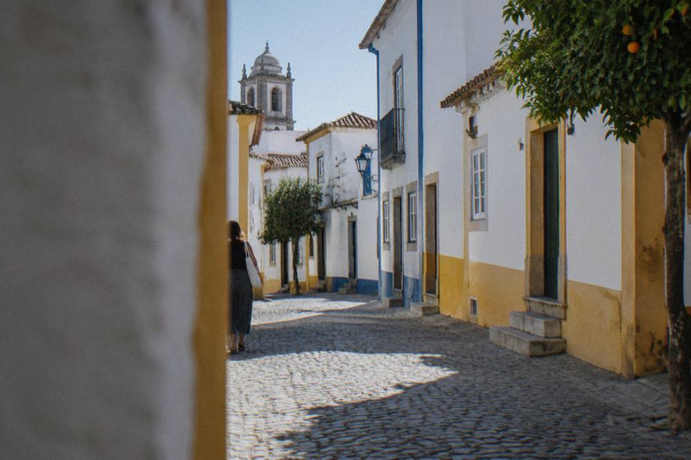 A shaded cobbled street in Évora with white houses and blue and yellow trim offering relief from the midday sun