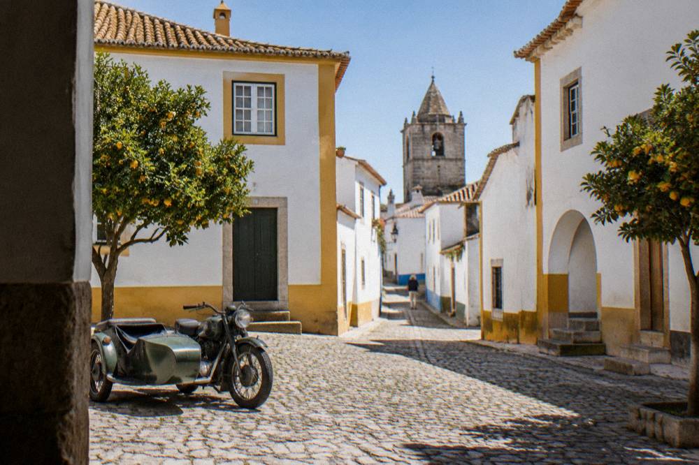 A vintage sidecar motorcycle parked on a cobbled square in Évora beside whitewashed buildings