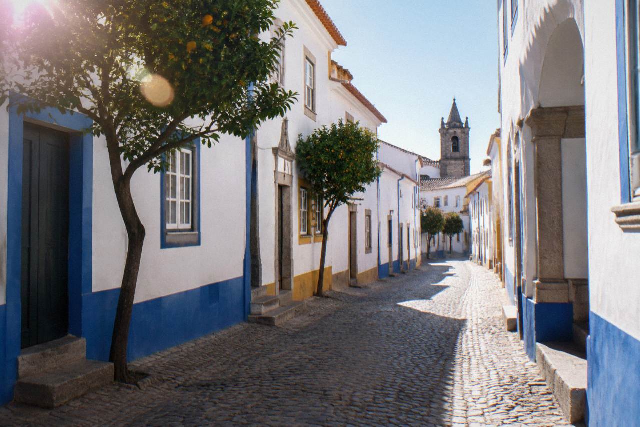 Sunlit narrow street in the walled historic centre of Évora with white houses and blue trim