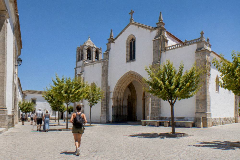 Tourists walking through a sunlit square near the Igreja de São Francisco in Évora