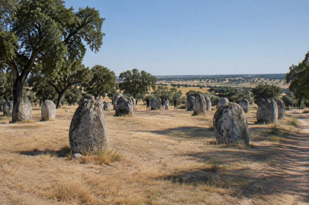 Visitors standing among the standing stones of the Almendres cromlech near Évora at sunset