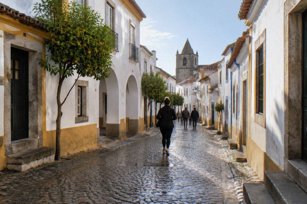 Travellers walking a narrow cobbled street lined with white-walled houses in Évora's historic centre