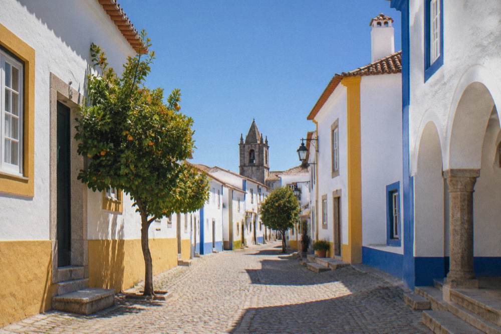 A whitewashed Évora street with blue and yellow trim glowing under strong late-afternoon sun