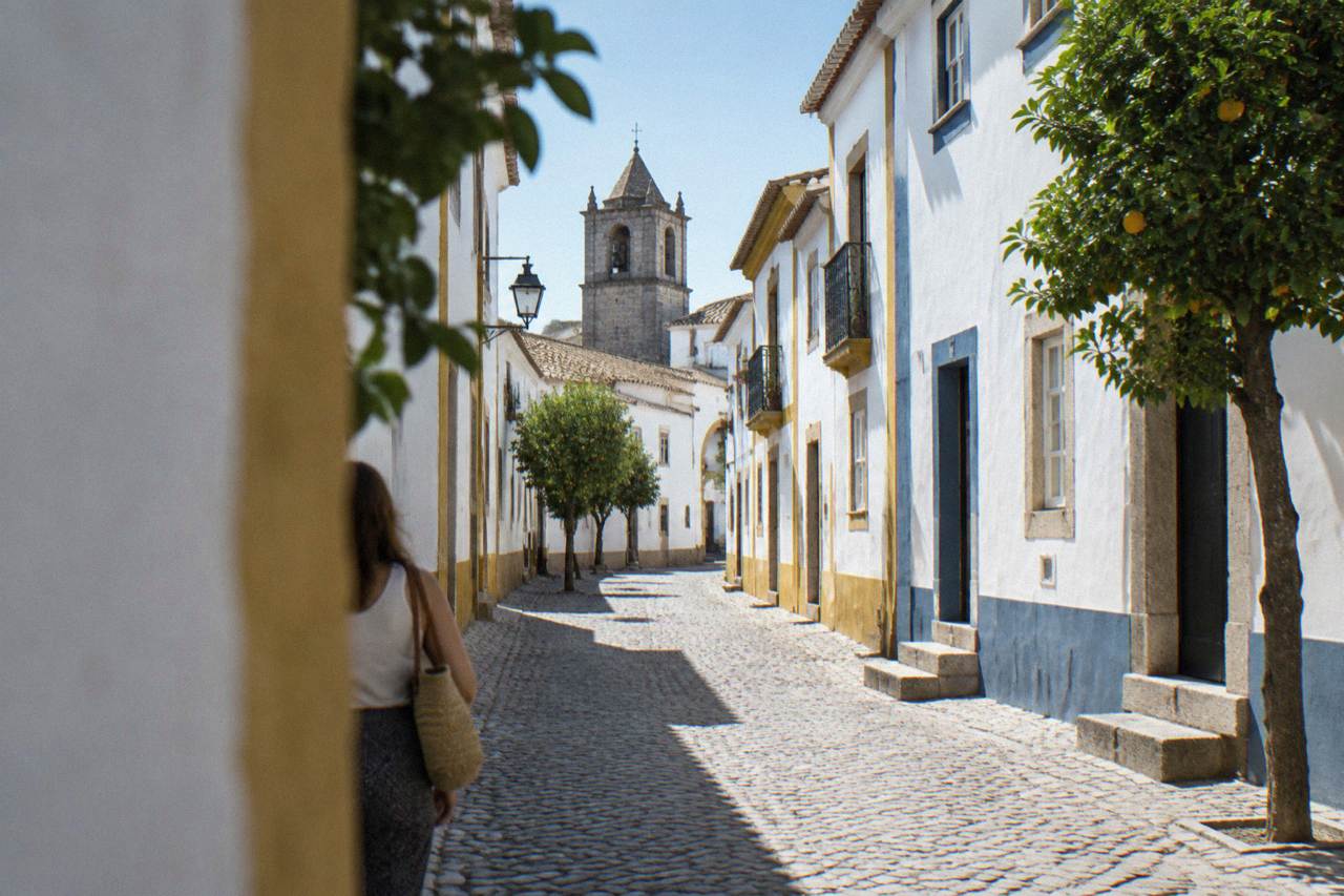 A quiet cobbled street in the historic centre of Évora with whitewashed apartment buildings and blue and yellow trim