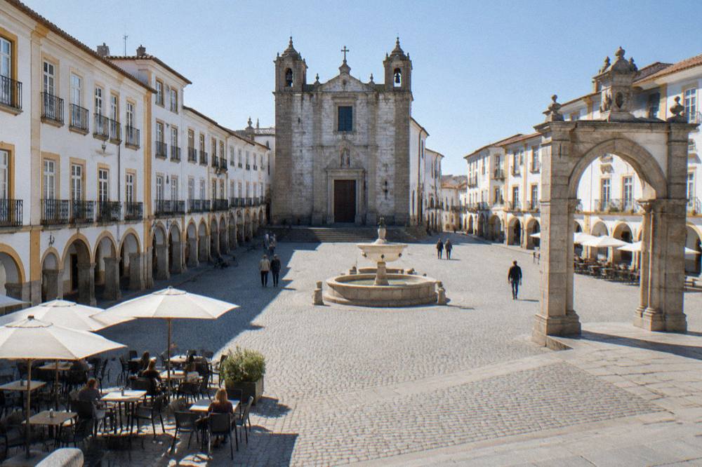 Sunlit square in Évora with café tables and the Renaissance arch of Praça do Giraldo