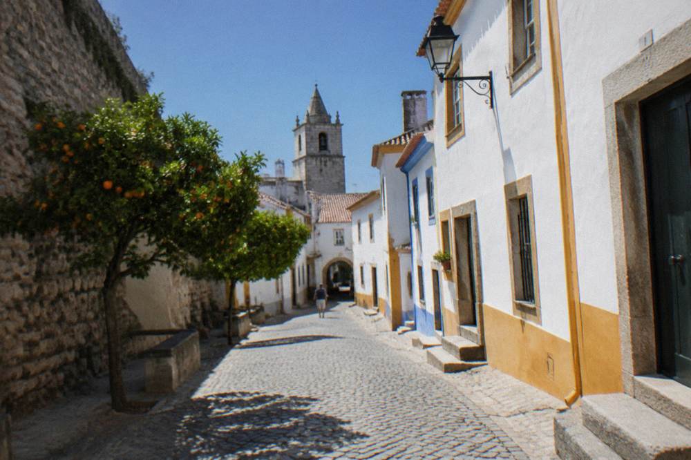 A stretch of old stone wall in Évora with houses built against it and a narrow lane alongside