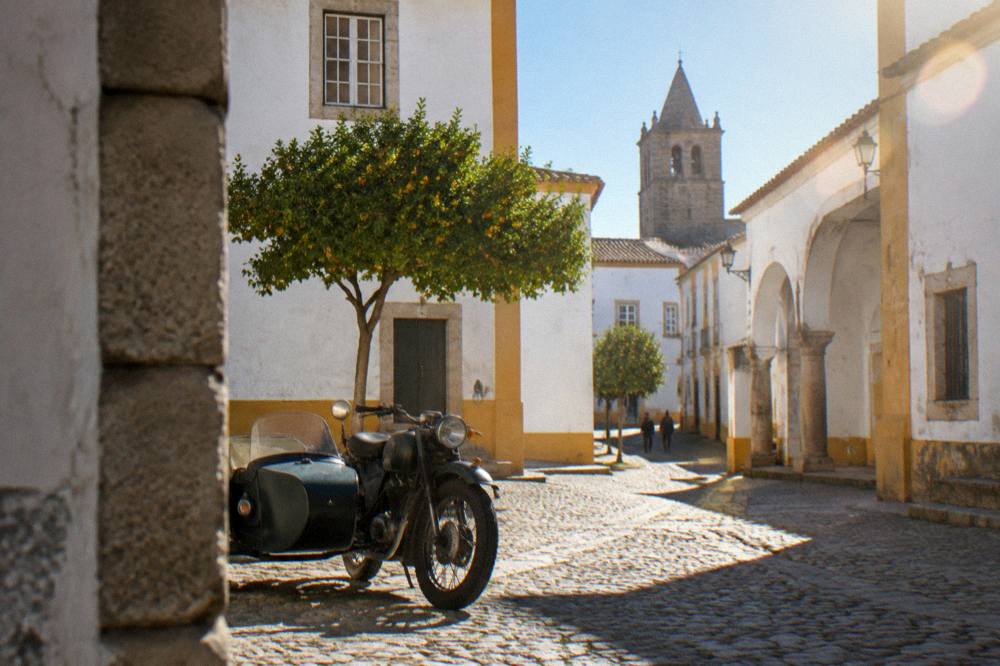 A classic motorcycle sidecar parked on a cobbled square in Évora beside old stone buildings