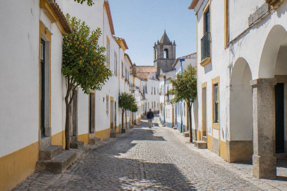 White-washed houses along a narrow cobbled street in Évora under strong sunlight