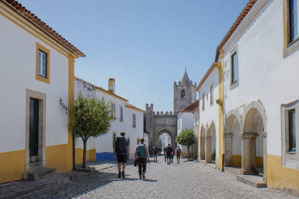 Travellers with backpacks walking away from a coach terminal toward a historic town gate