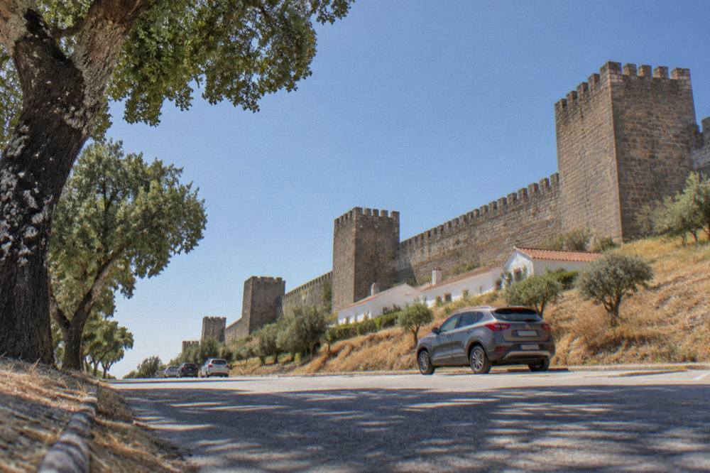 A rental car parked on a quiet Alentejo road lined with cork oak trees under a wide sky