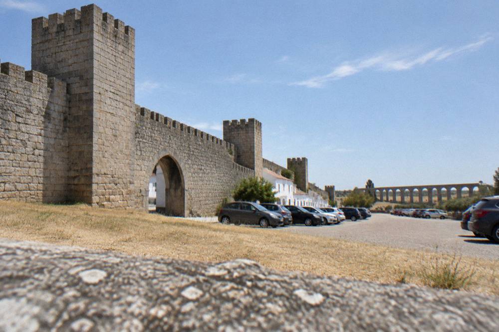 Cars parked in a open-air car park outside the medieval walls of Évora with the aqueduct visible in the distance